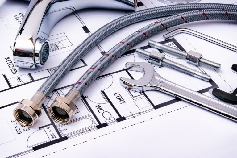 Plumbing tools and a faucet supply line laid on a house blueprint